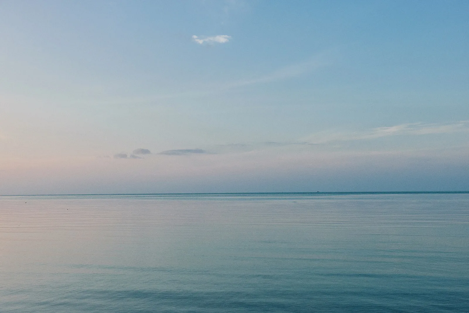 A calm sea meeting a soft blue sky at Bang Kao Beach