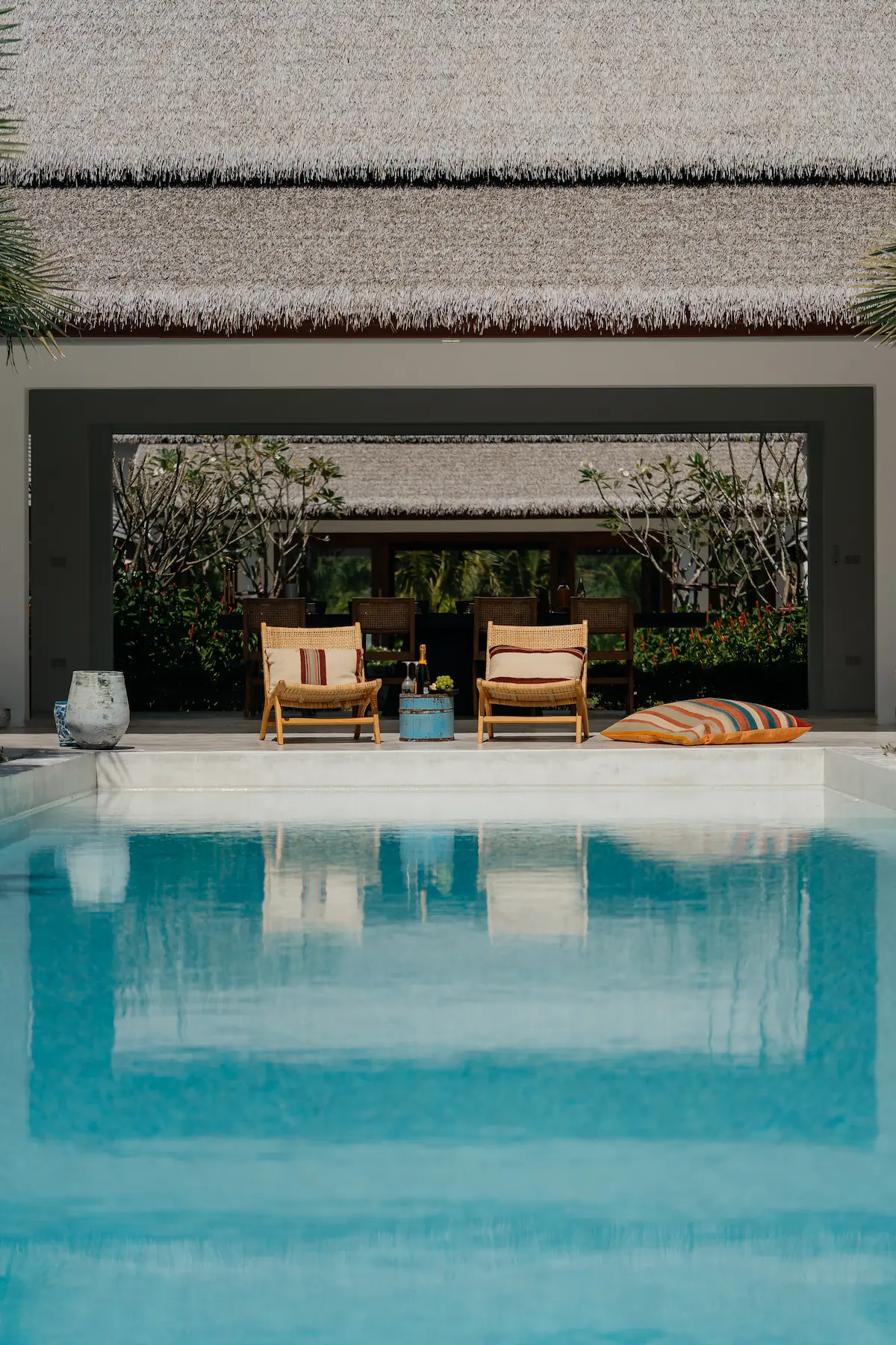 Rattan lounge chairs with cushions by the pool under thatched roof pavilion at Villa Aditi, Koh Samui
