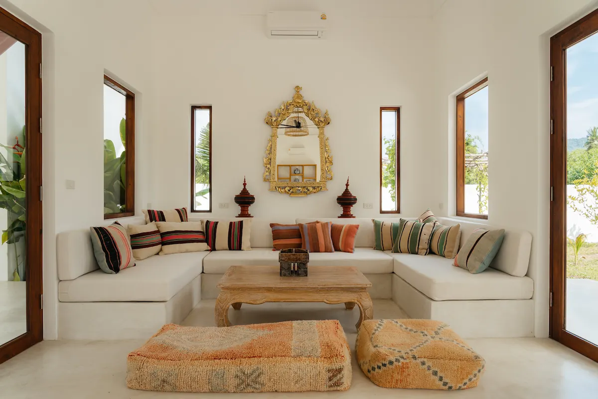 Air-conditioned lounge with ornate gilded mirror, striped cushions, and floor poufs at Villa Aditi, Koh Samui