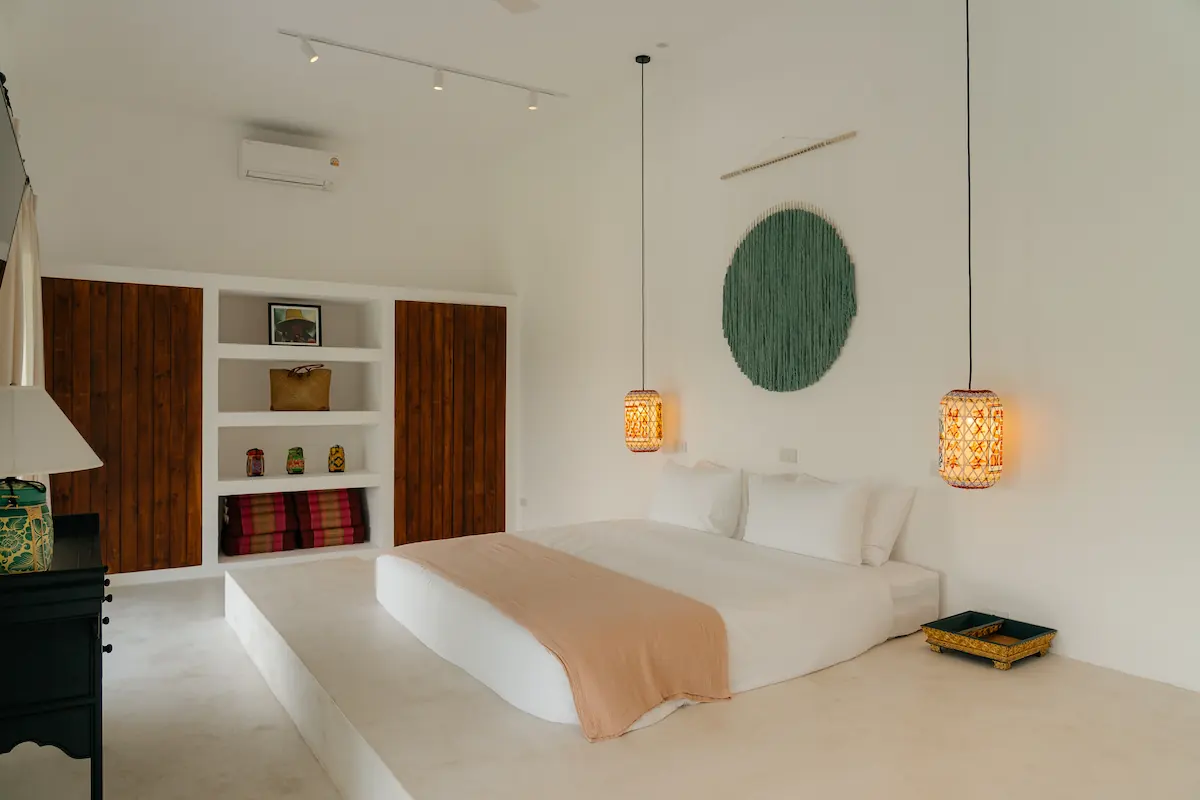 King-size platform bed with woven pendant lamps, teal wall art, and wooden dressing area at Villa Aditi, Koh Samui